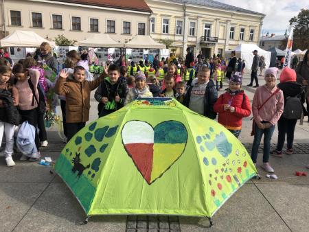 Uczniowie stoją na rynku w Kielcach, prezentują swoją pracę konkursową.