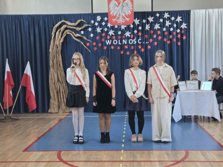 4 uczennice stoją na scenie, jedna recytuje wiersz