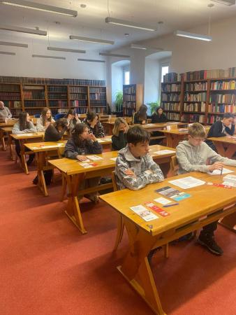 Uczniowie w bibliotece na wykładzie siedzą w ławkach
