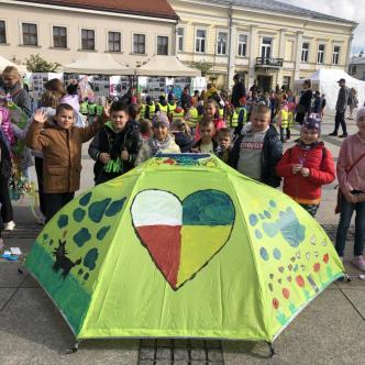 Uczniowie stoją na rynku w Kielcach, prezentują swoją pracę konkursową.