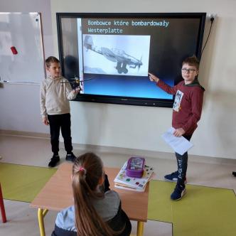 Uczniowie klasy 3b prowadzą lekcje historii przy tablicy multimedialnej w sali lekcyjnej.