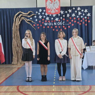 4 uczennice stoją na scenie, jedna recytuje wiersz