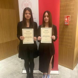 Uczennice sp12 z dyplomami na tle flagi Polski