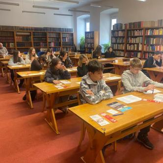 Uczniowie w bibliotece na wykładzie siedzą w ławkach